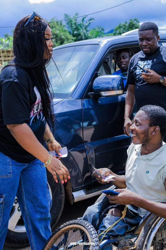 Roseline Layo qui donne de l'argent à un handicapé 